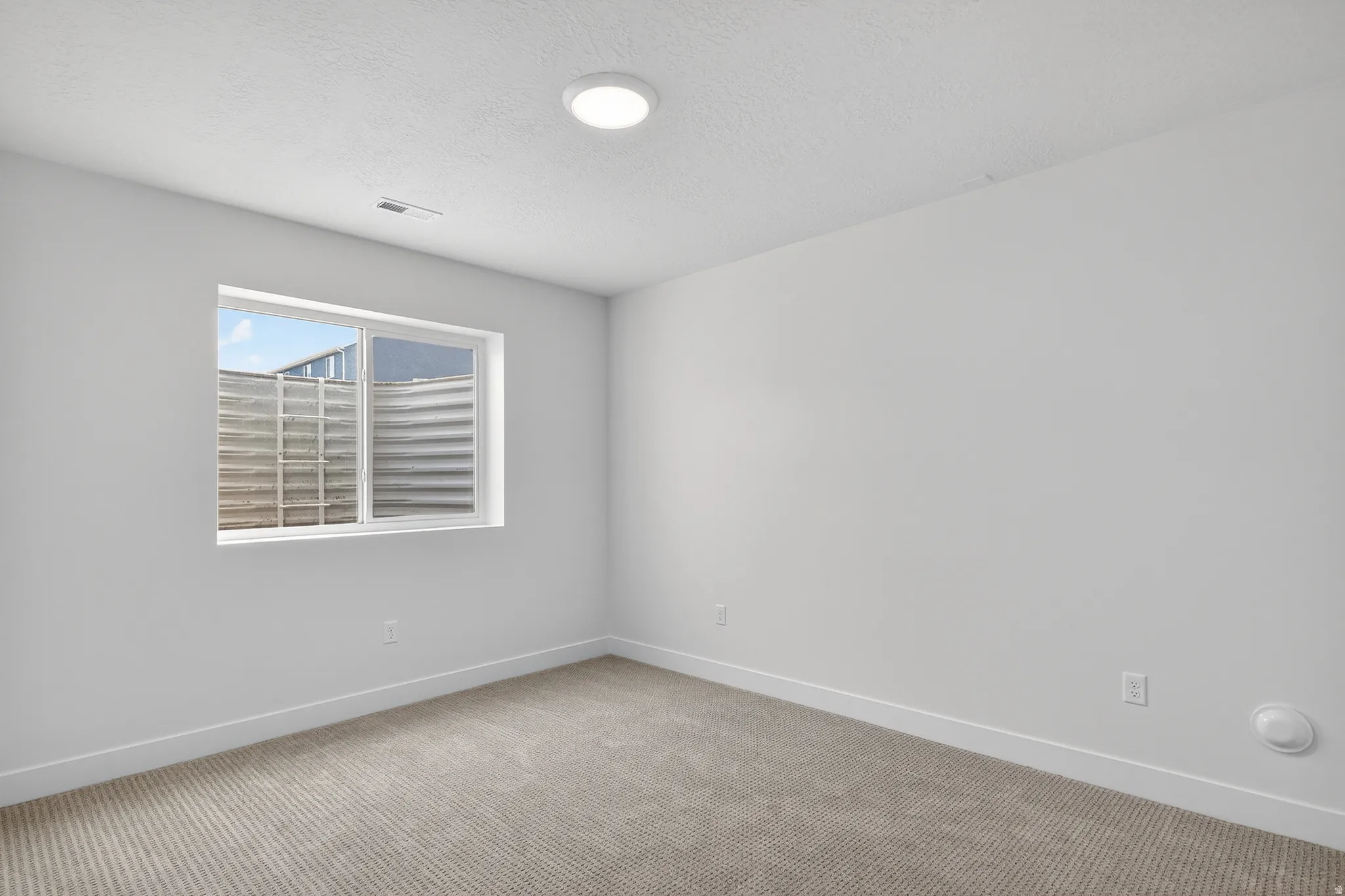 Empty room with light carpet and a textured ceiling
