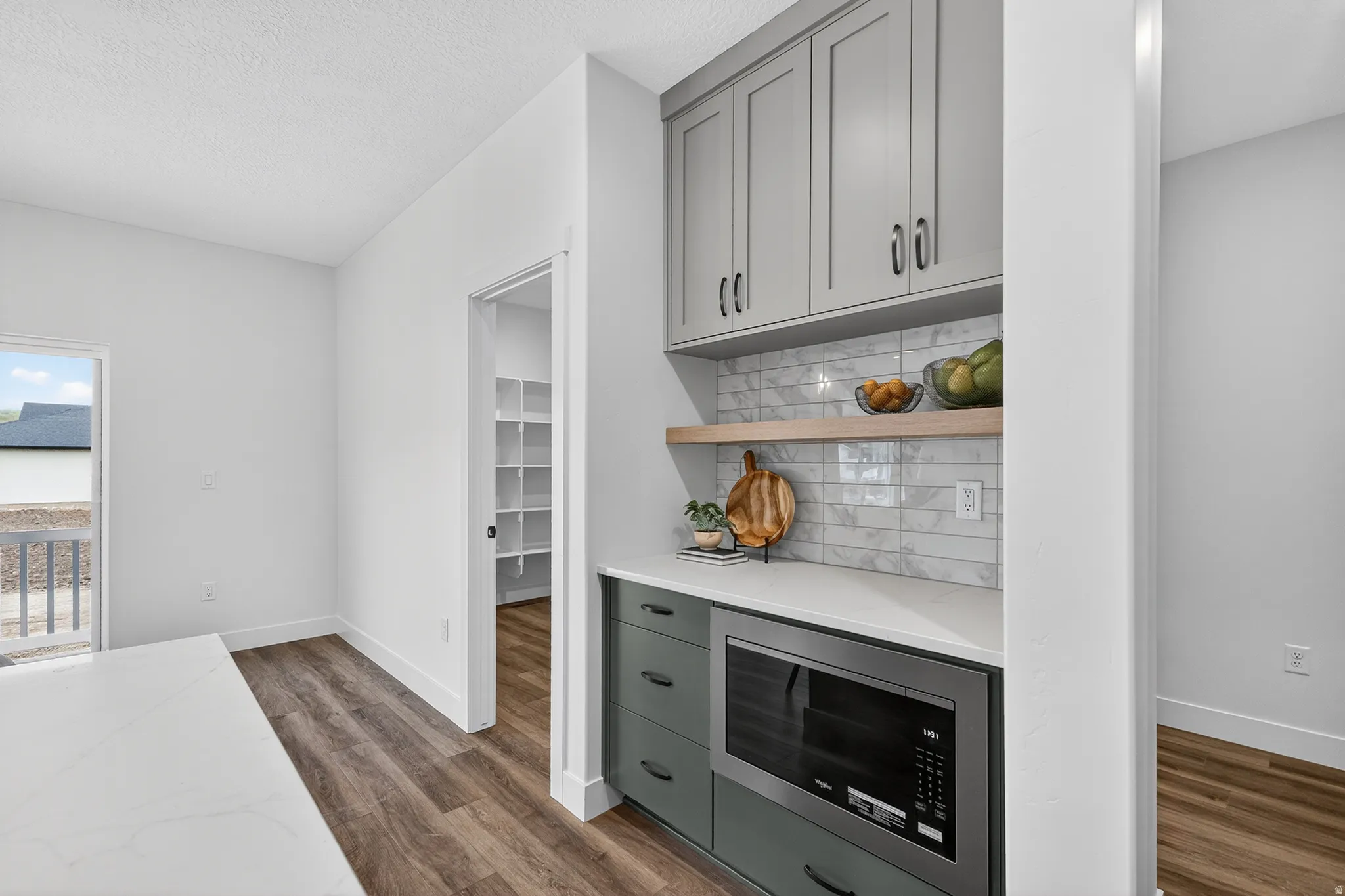 Bar area with stainless steel microwave, open shelves, gray cabinets, dark wood finished floors, and light stone counters