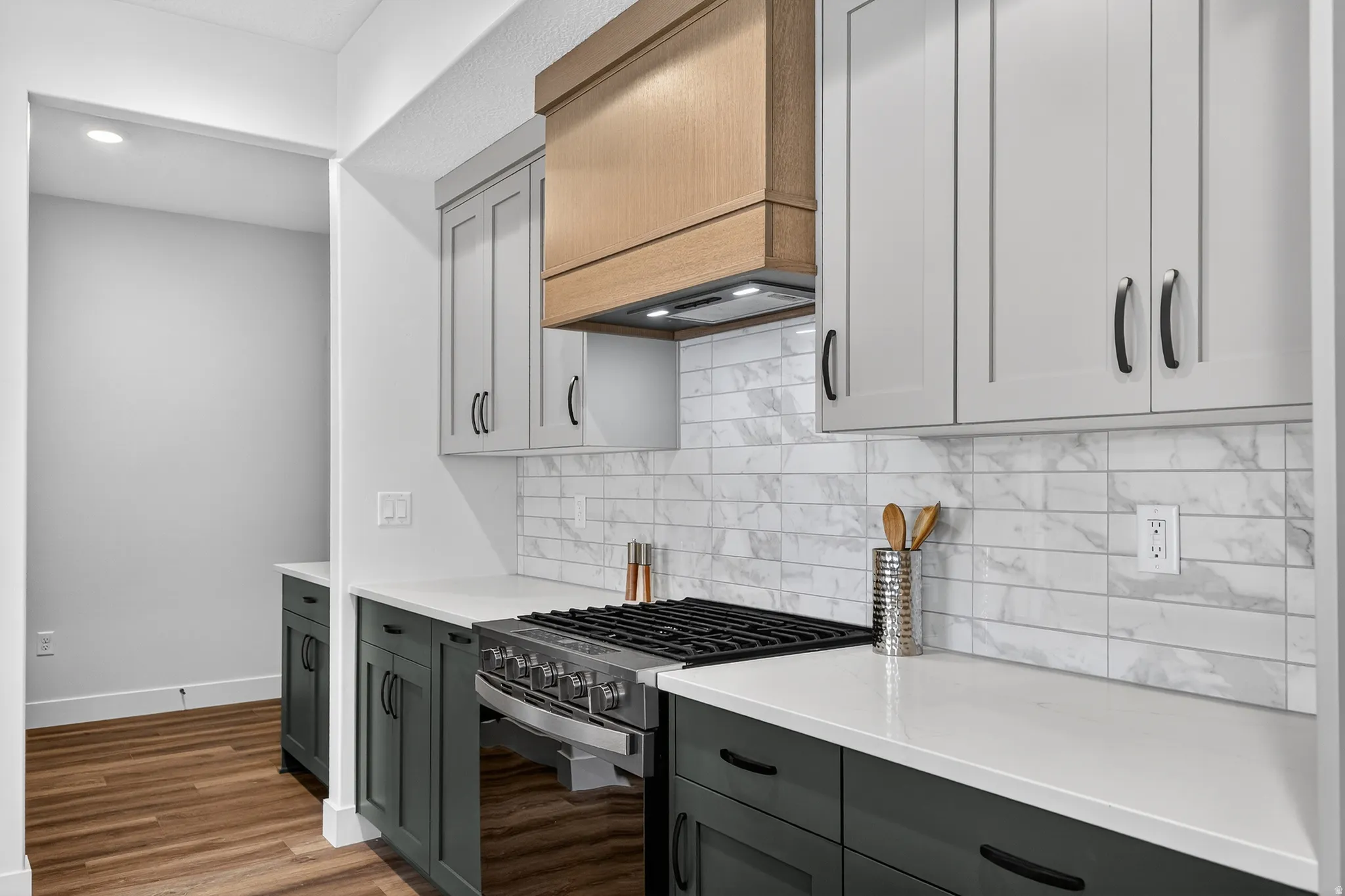 Kitchen with gas range oven, light wood-type flooring, light stone counters, tasteful backsplash, and two tone cabinetry