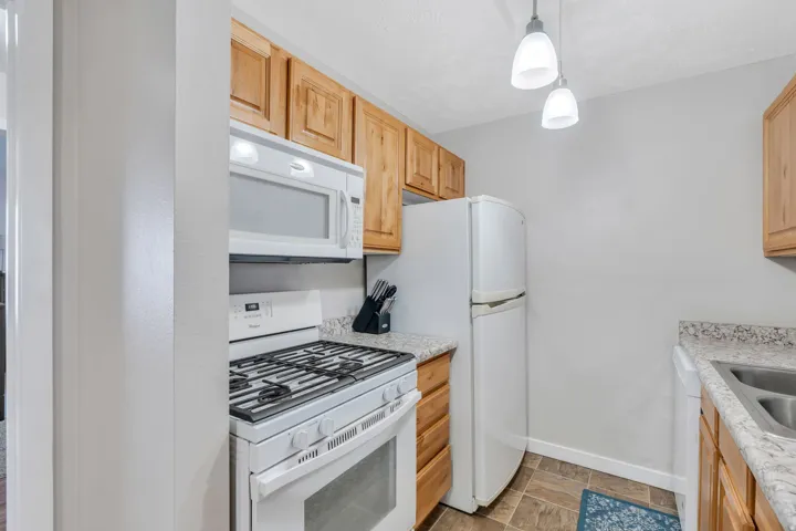 Kitchen with white appliances, decorative light fixtures, and light stone counters