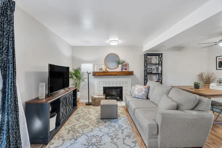 Living room with a tiled fireplace, ceiling fan, and light wood-type flooring