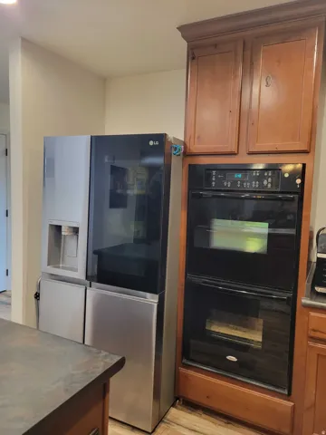Kitchen featuring stainless steel fridge with ice dispenser, wood finish cabinets, light wood-style flooring, Double oven and dark countertops