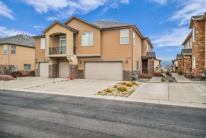 View of front of house with stone siding, an attached garage, stucco siding, and driveway