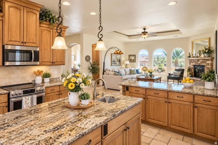 Open-concept kitchen and living area featuring granite countertops, wood cabinetry, stainless steel appliances, and arched windows