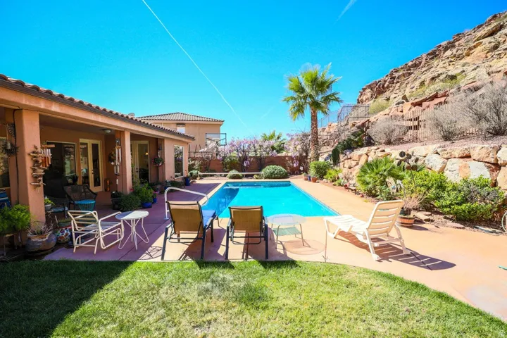 Expansive backyard featuring a blue-tiled swimming pool, a covered patio area, and a stone retaining wall