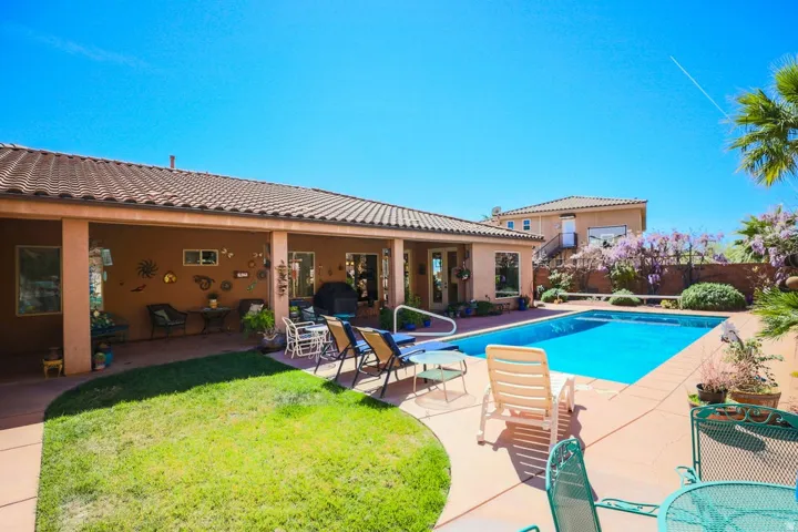 In-ground swimming pool, expansive paved patio, covered outdoor living area, manicured lawn, and mature landscaping