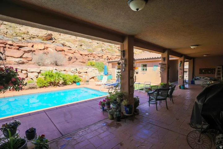 Expansive covered patio with recessed lighting and stamped concrete flooring, featuring a rectangular in-ground pool and surrounding rock landscaping