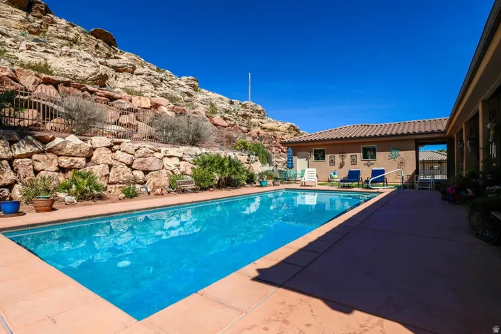 Rectangular inground swimming pool with a surrounding concrete patio, rock retaining wall, and mature landscaping