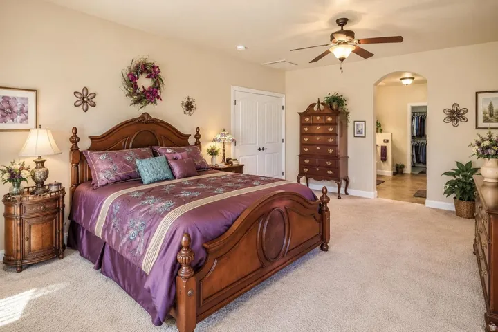 Carpeted flooring, vaulted ceiling, ceiling fan, white paneled door, and an arched entryway leading to a walk-in closet