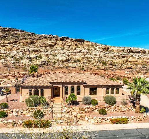 Southwestern-style architecture featuring a tile roof, stucco exterior, multiple arched windows, and a tiered rock wall landscape
