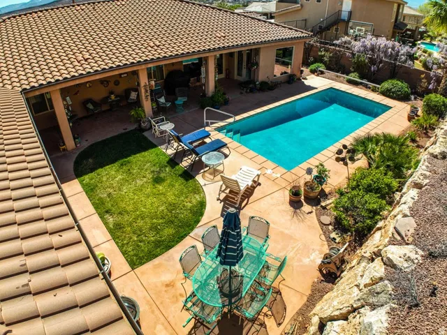 Outdoor pool area featuring a rectangular swimming pool, concrete patio, covered patio, and a terraced rock wall