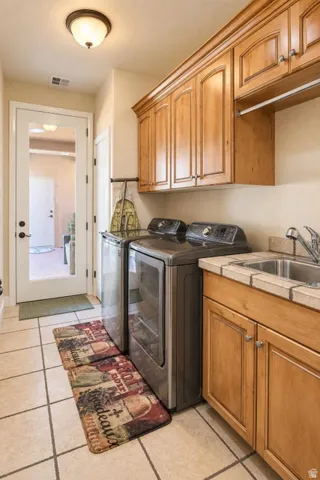 Utility room with light wood-finish cabinetry, a tile countertop, and an integrated sink
