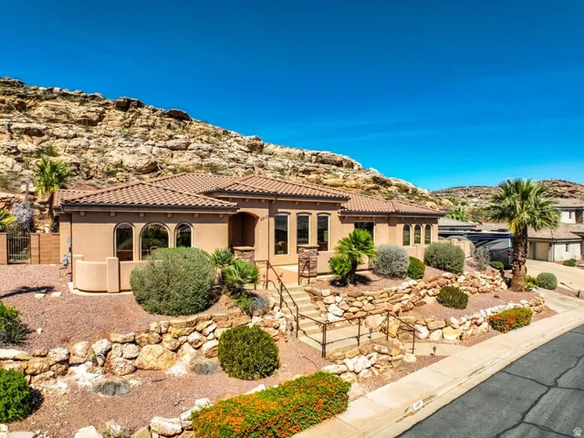 Stucco exterior with a tile roof, arched windows, tiered landscaping featuring rock walls, and a prominent mountain backdrop