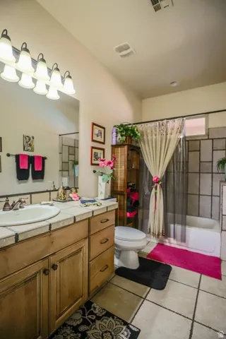 Wood-finish vanity with an integrated sink, tile countertop, and a shower-over-tub combination with tile surround