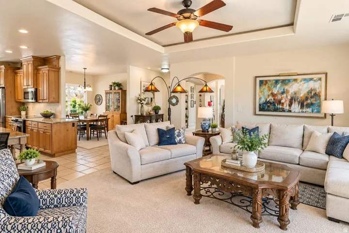 Open-concept living area with tray ceiling, ceiling fan, and carpet flooring