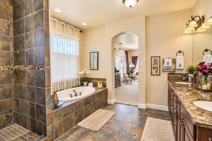 Recessed soaking tub with surrounding tile, separate tile shower with decorative accent band, and dual vanity with stone countertop and individual sinks