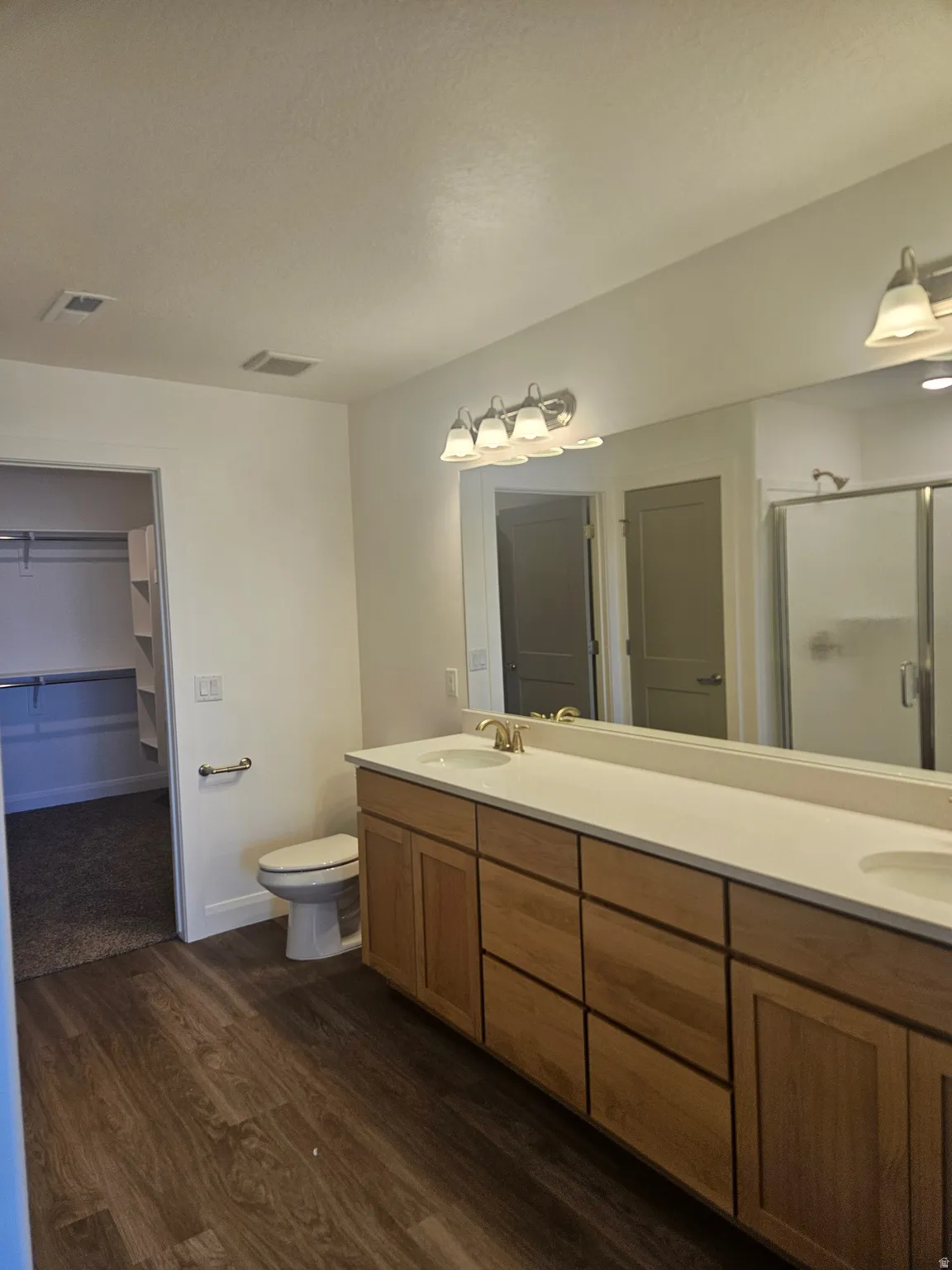 Full bathroom featuring a walk in closet, double vanity, a shower stall, and dark wood-type flooring