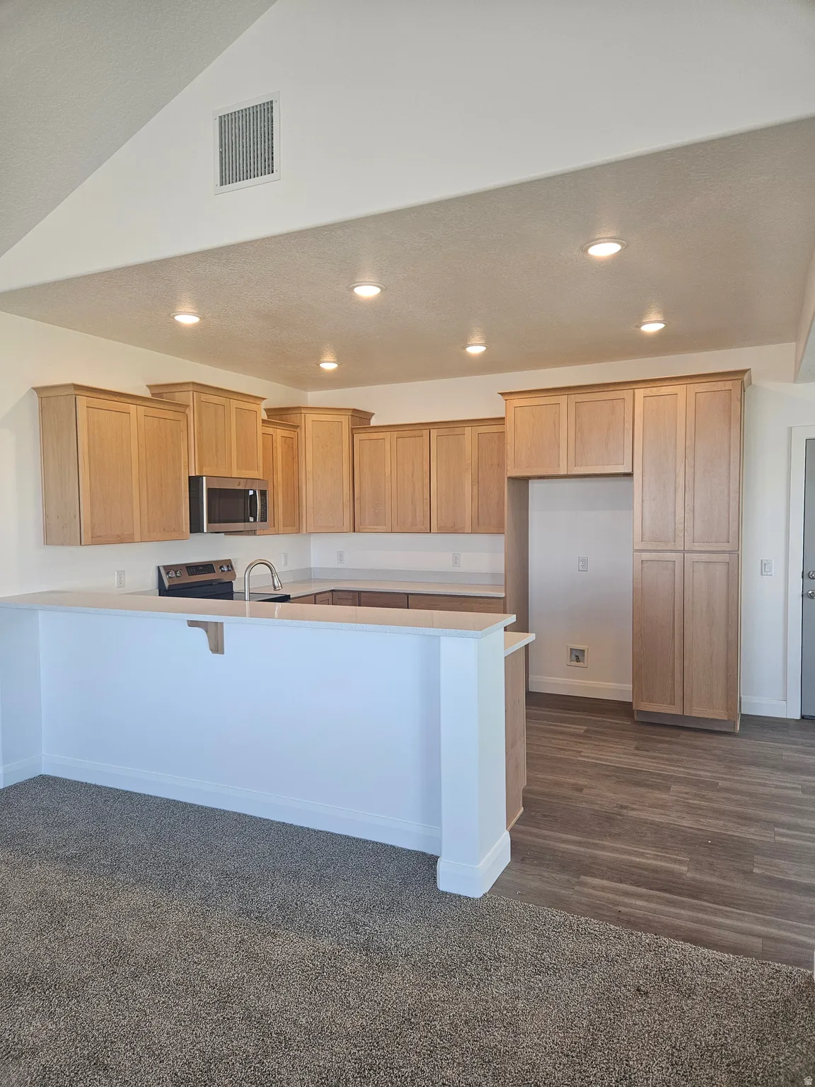 Kitchen with a peninsula, a breakfast bar area, light countertops, stainless steel appliances, and recessed lighting
