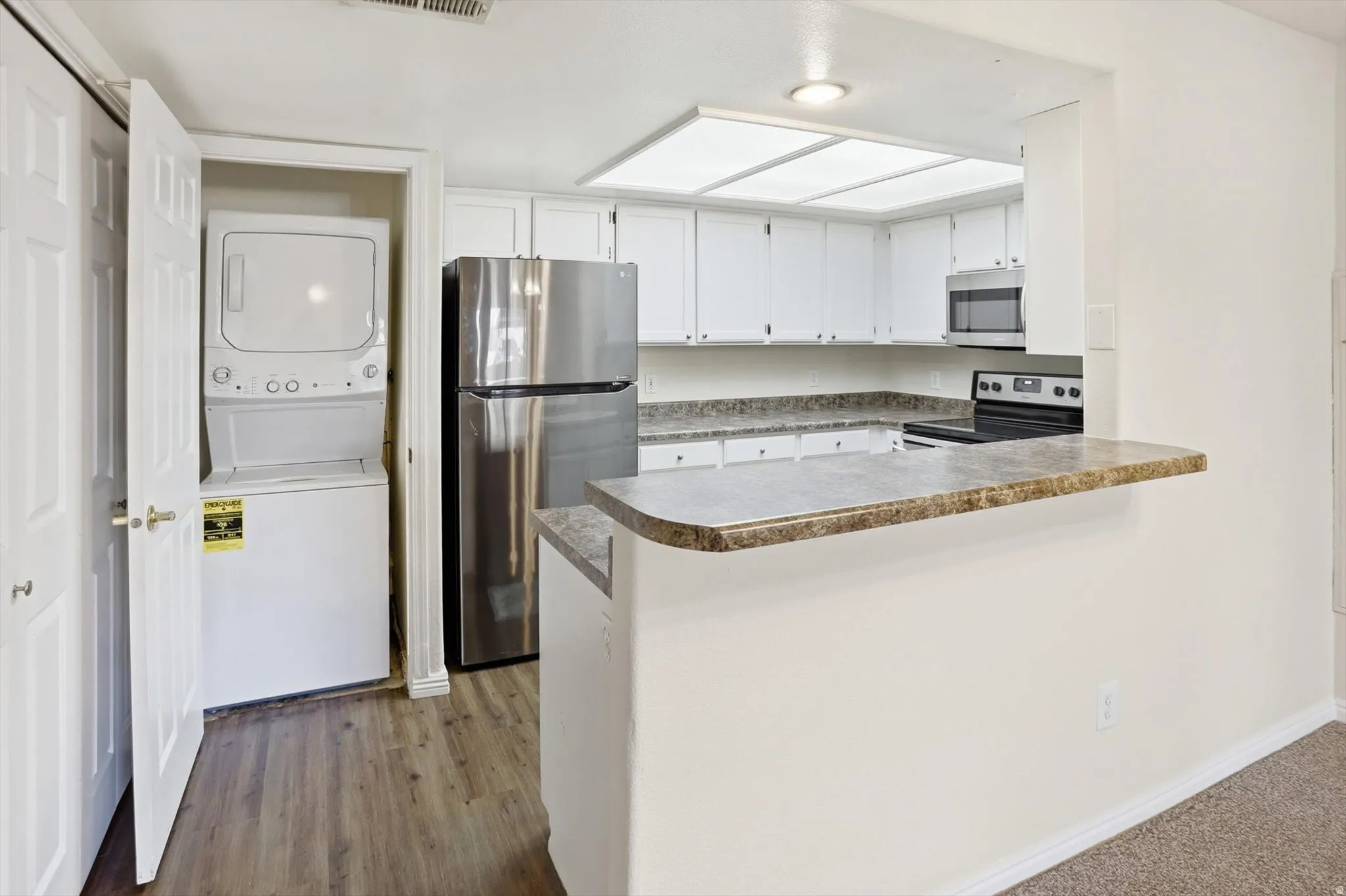 Kitchen with white cabinetry, stainless steel appliances, a peninsula, stacked washer / drying machine, and light wood-style flooring