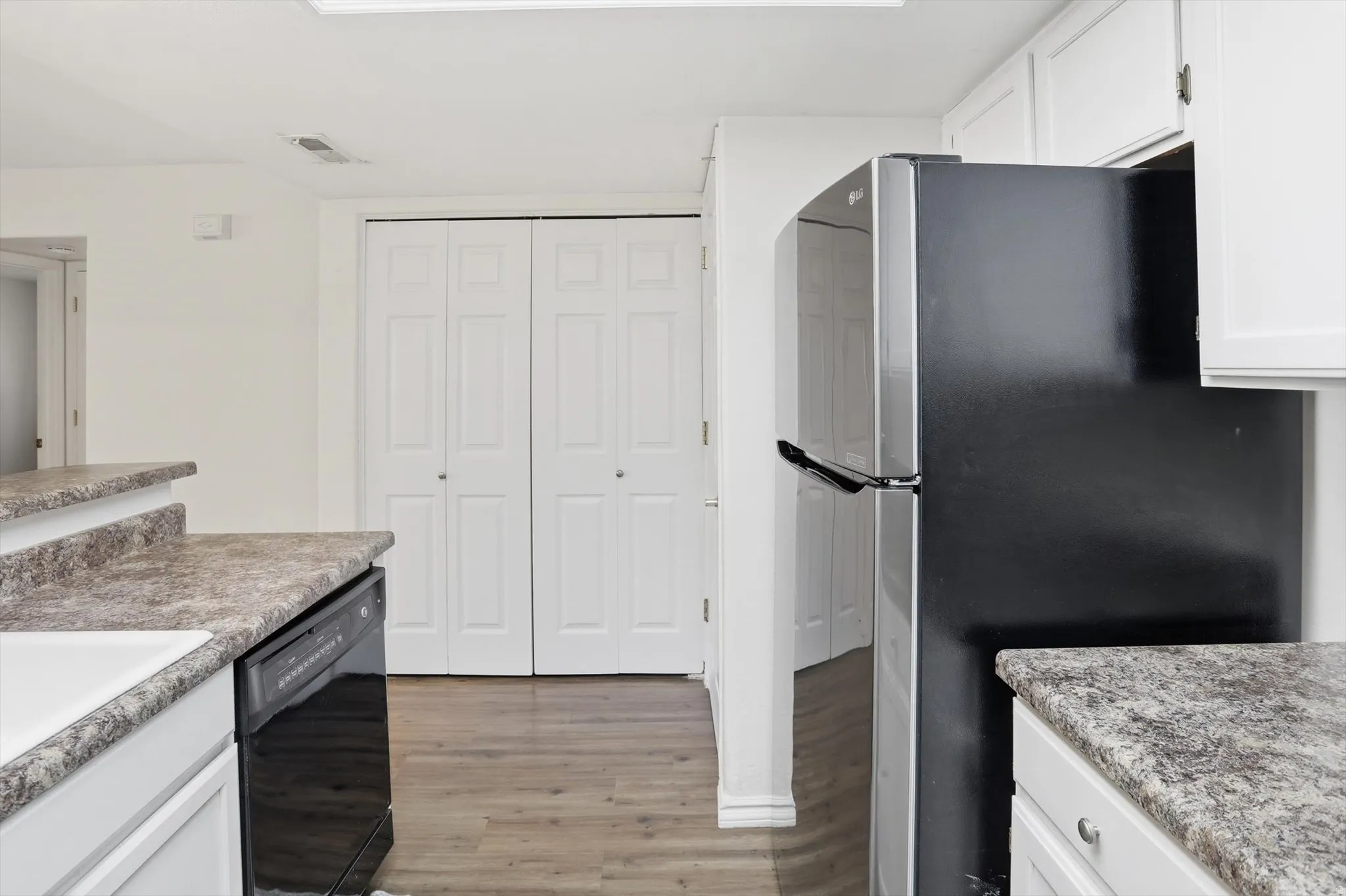 Kitchen with freestanding refrigerator, white cabinets, light wood-style flooring, dishwasher, and light countertops