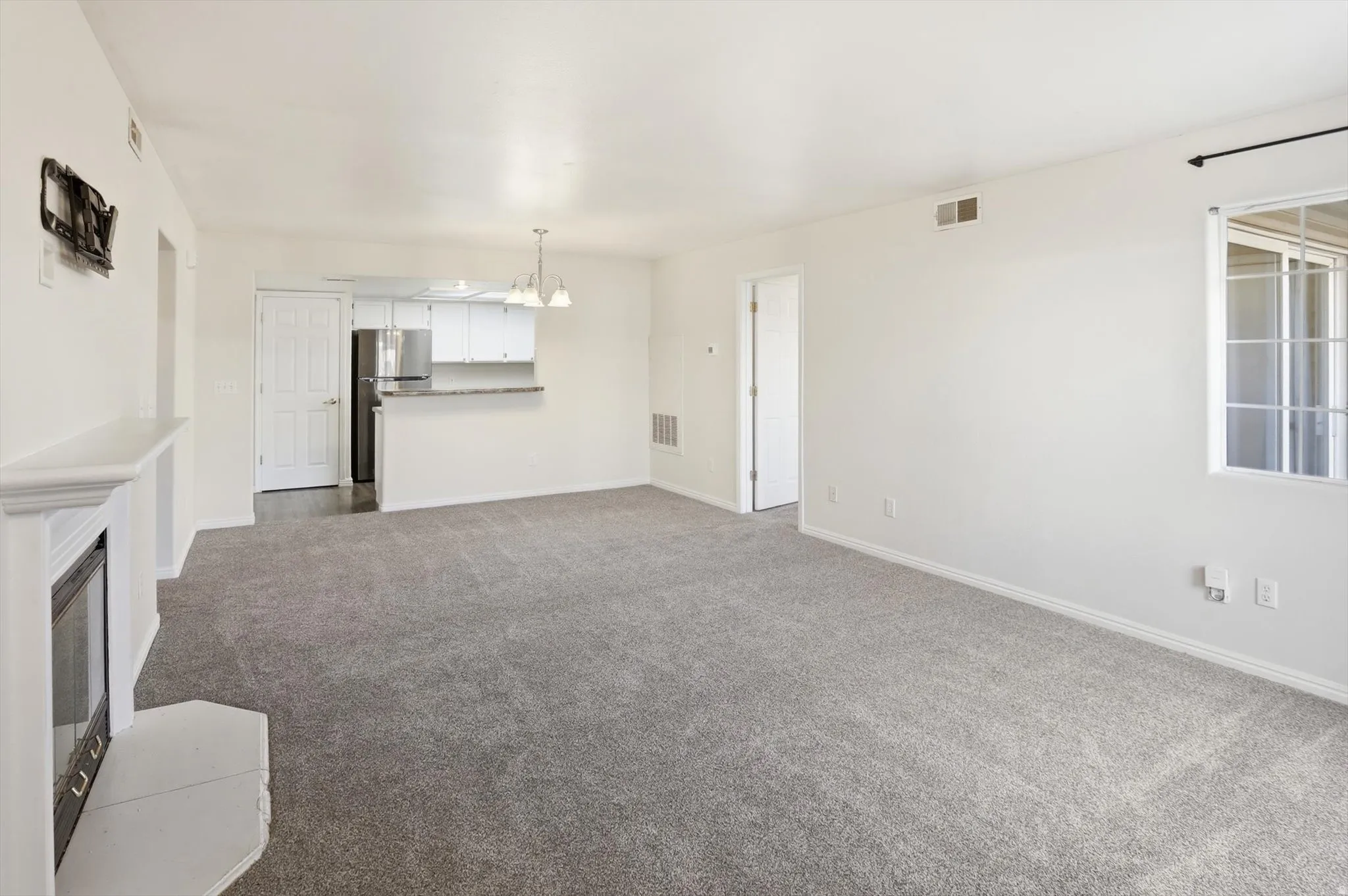 Unfurnished living room with dark colored carpet, hanging lights, and a glass covered fireplace