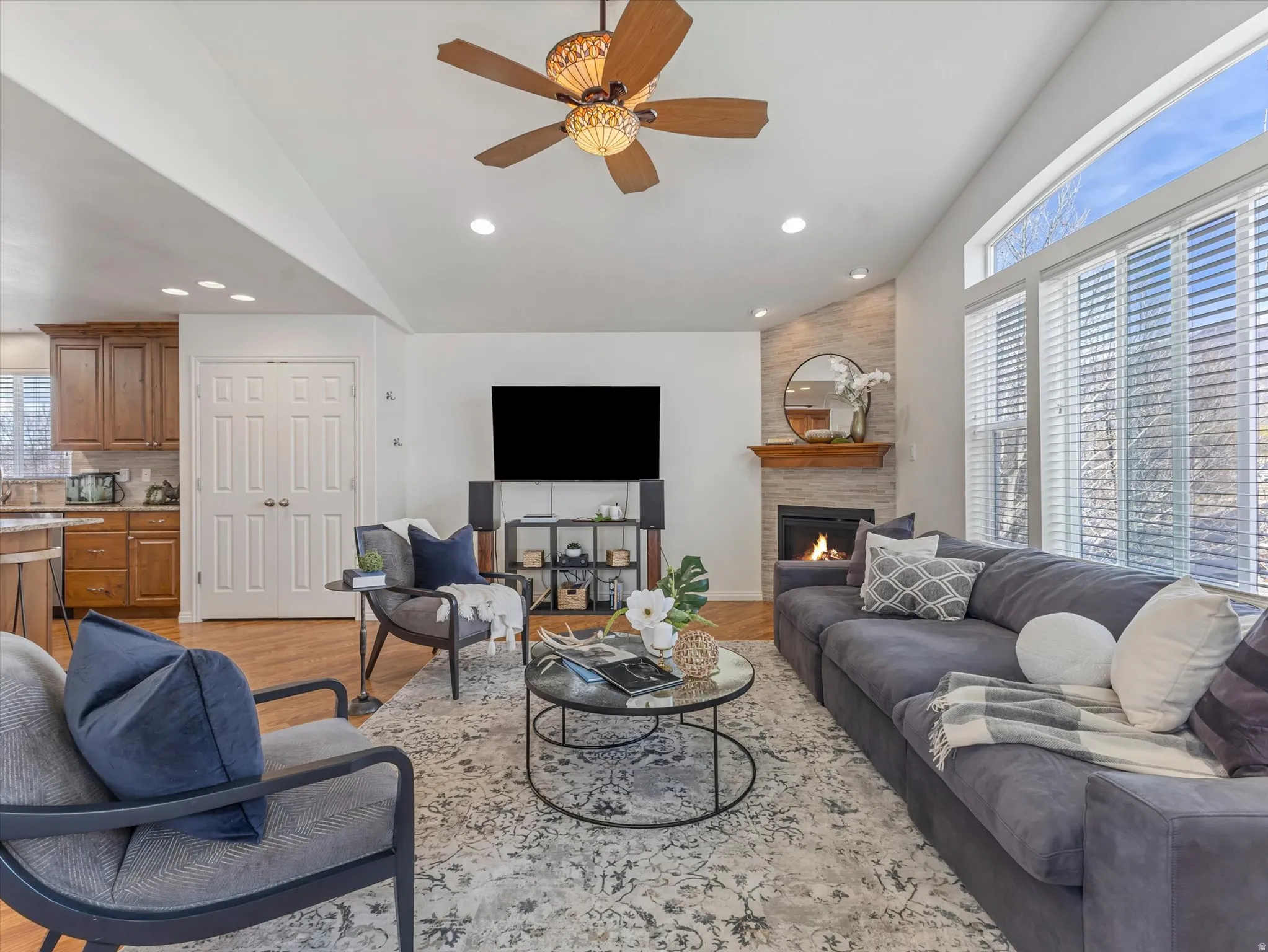 Living room with light wood-style flooring, lofted ceiling, a ceiling fan, a large fireplace, and recessed lighting