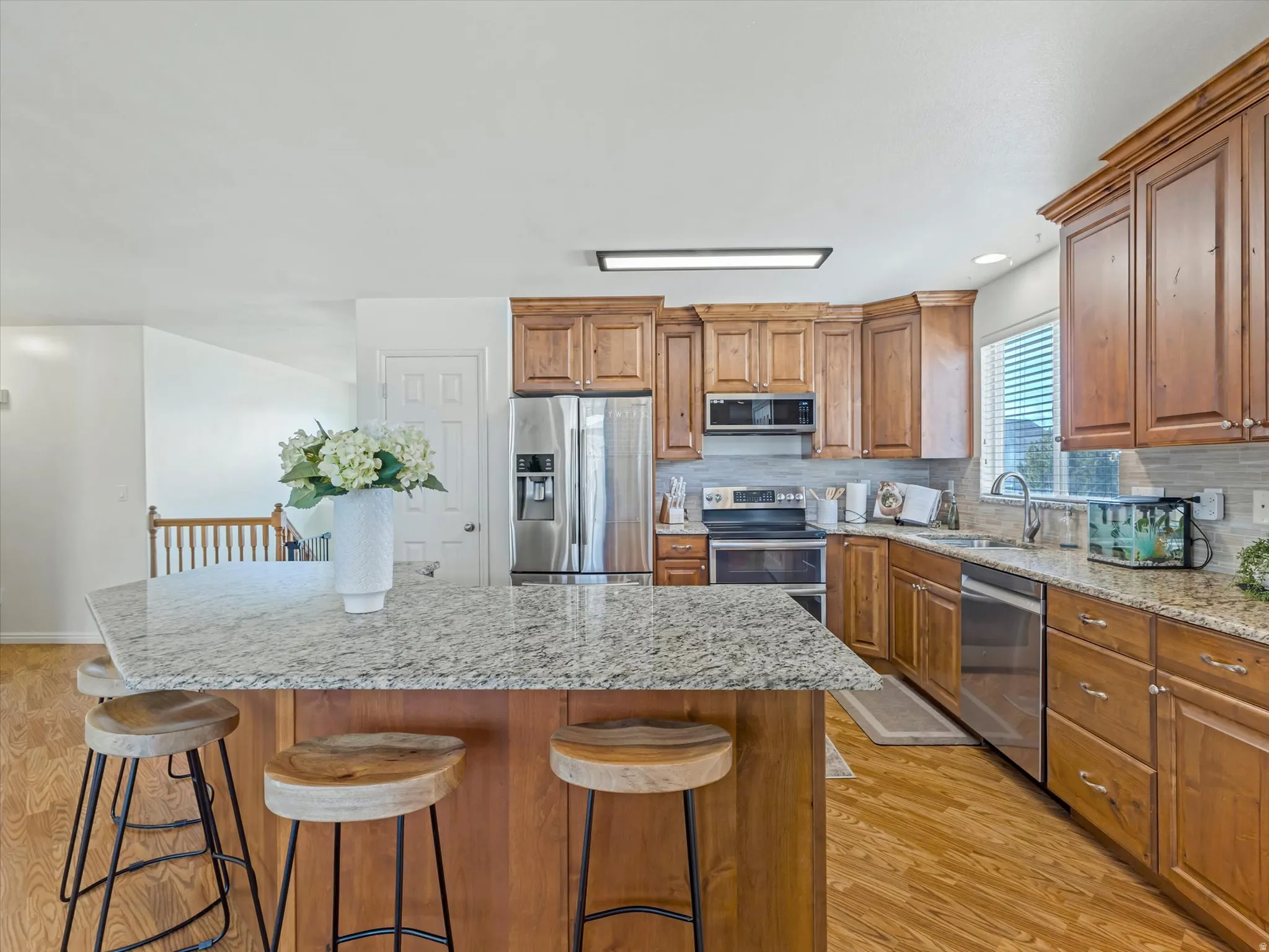 Kitchen with light stone counters, wood finish cabinets, stainless steel appliances, light wood finished floors, and recessed lighting