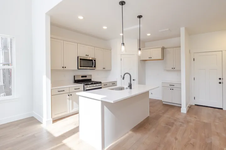 Modern kitchen featuring light cabinetry, stainless steel appliances, a center island with sink, and pendant lighting