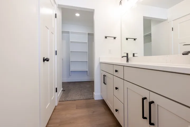 Bathroom vanity featuring light-toned cabinetry, a solid surface countertop, matte black hardware, and an integrated mirror