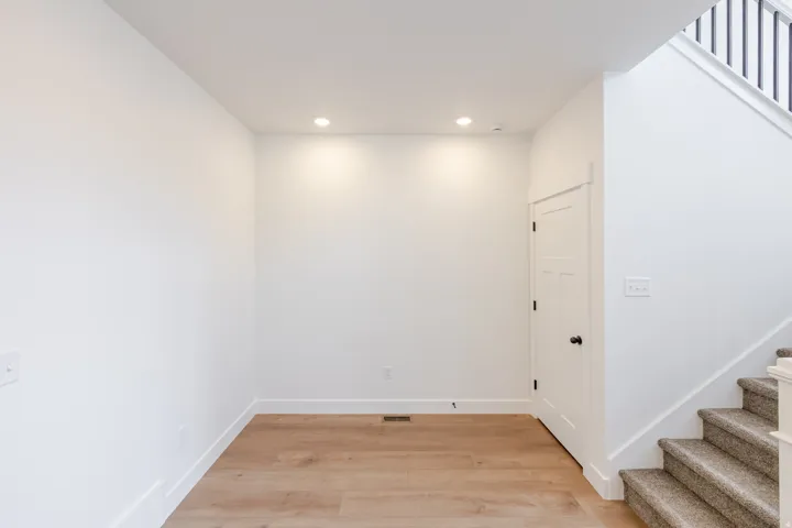Entryway featuring recessed lighting, wood-finish flooring, a white paneled door, and a carpeted staircase with dark balusters
