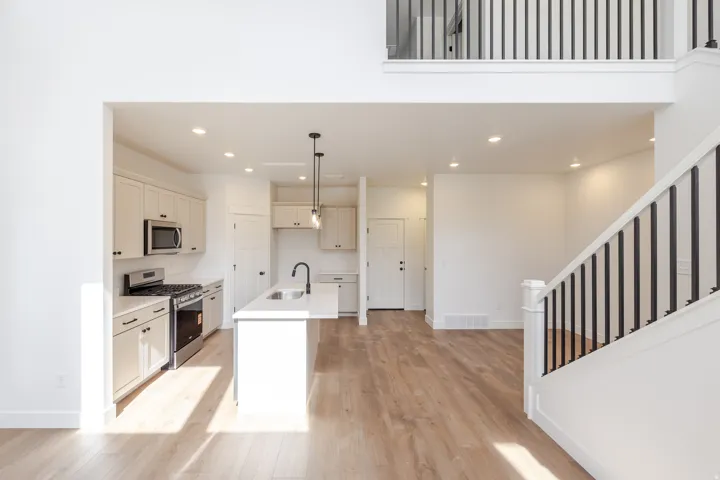 Open-concept living space with wood-finish flooring, a contemporary kitchen, and a staircase featuring black metal balusters