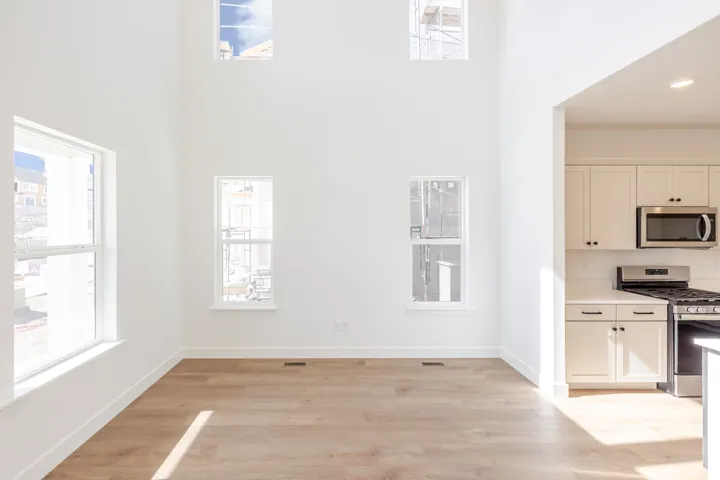 Vaulted ceilings with multiple windows, wood-finish flooring, and an open concept layout with a kitchen featuring white cabinetry, a gas range, and a microwave