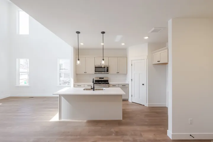 Open-concept living space featuring a kitchen island with seating, pendant lighting, stainless steel appliances, and wood-finish flooring