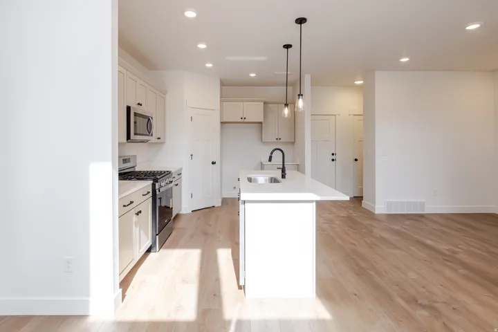 Kitchen featuring light-toned cabinetry, stainless steel appliances, a white subway tile backsplash, and a central island with a sink and pendant lighting