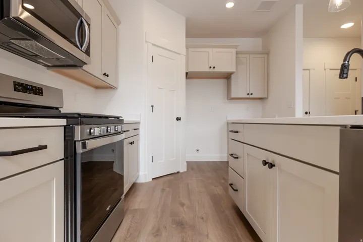 Contemporary kitchen featuring light wood-finish flooring, light-toned cabinetry with matte black hardware, stainless steel appliances, and solid surface countertops