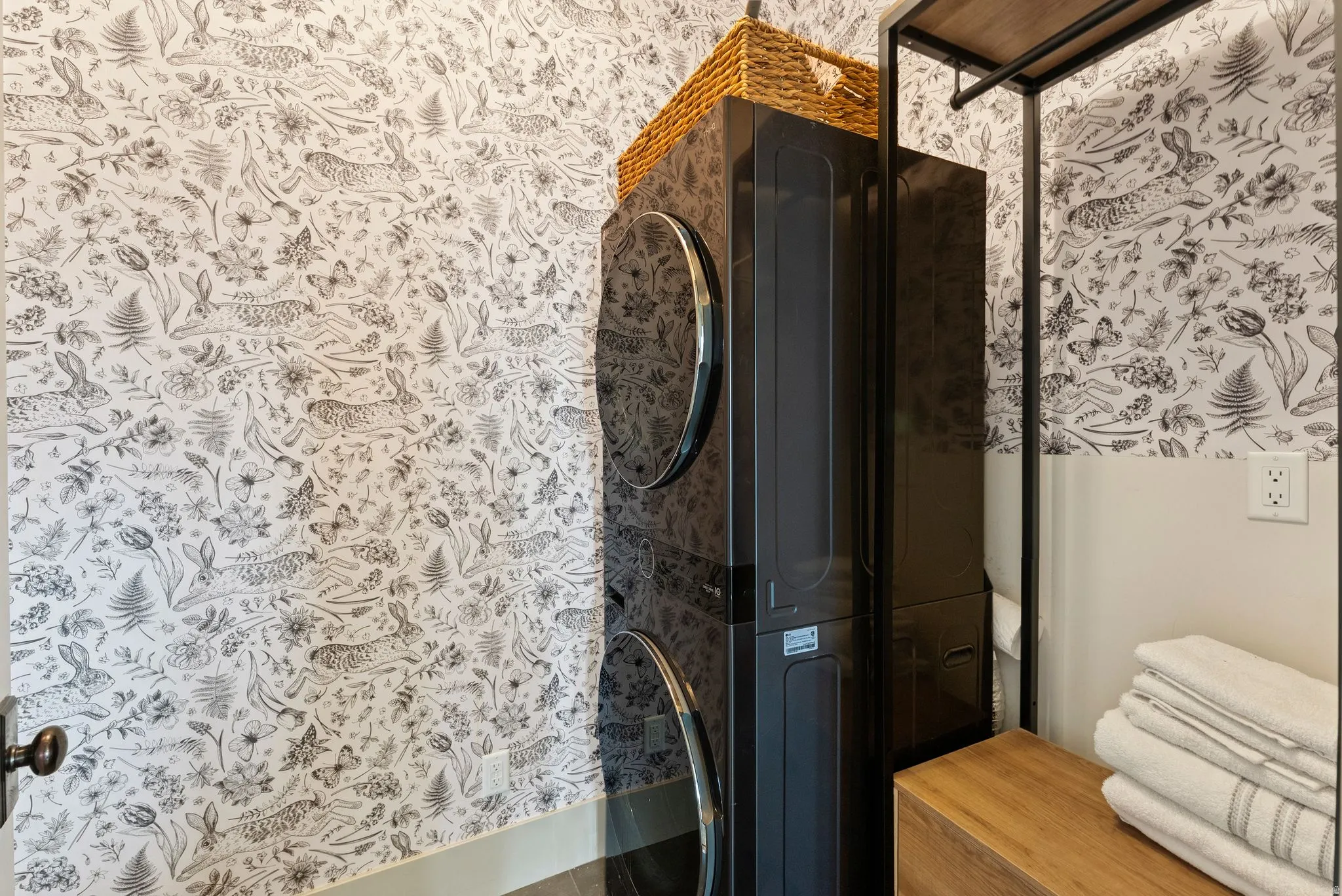 Bathroom with wallpapered walls, stacked washer / dryer, and a shower