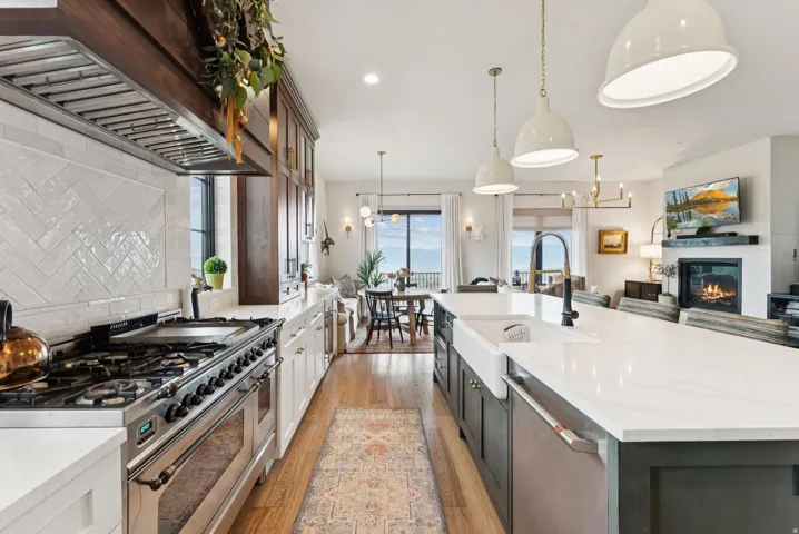 Kitchen with stainless steel appliances, two tone color scheme, light stone countertops, a glass covered fireplace, and a large island with sink
