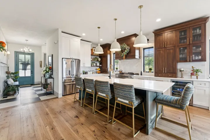 Kitchen featuring a breakfast bar, backsplash, stainless steel appliances, wine cooler, and a kitchen island with sink