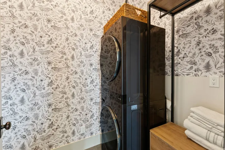 Bathroom with wallpapered walls, stacked washer / dryer, and a shower