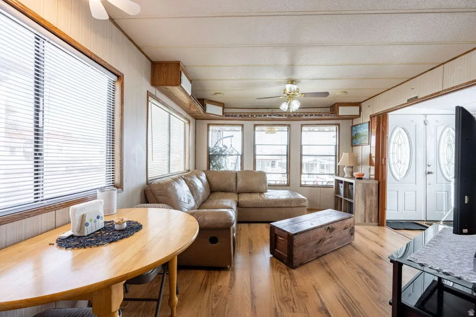 Living room featuring a ceiling fan, wooden walls, plenty of natural light, and light wood-style floors
