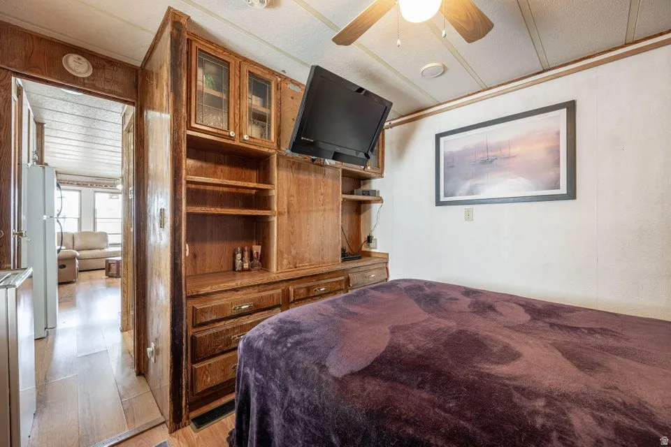 Bedroom featuring light wood-type flooring, freestanding refrigerator, a ceiling fan, and stainless steel refrigerator