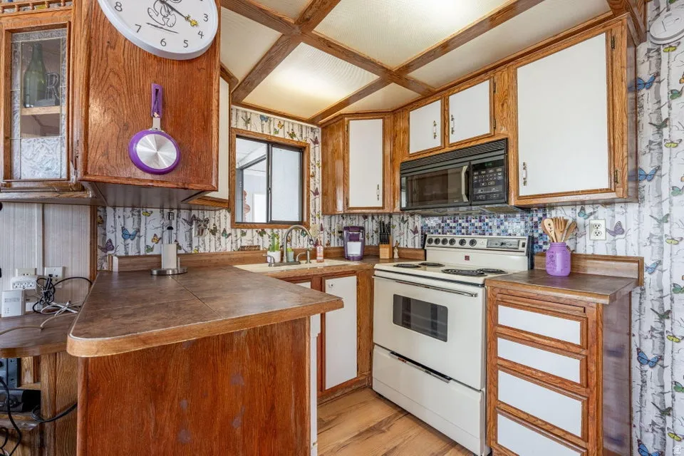 Kitchen with white electric stove, wallpapered walls, dark countertops, black microwave, and light wood-style flooring