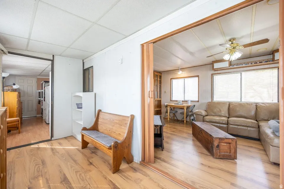 Living area with light wood-style flooring, a ceiling fan, and a paneled ceiling