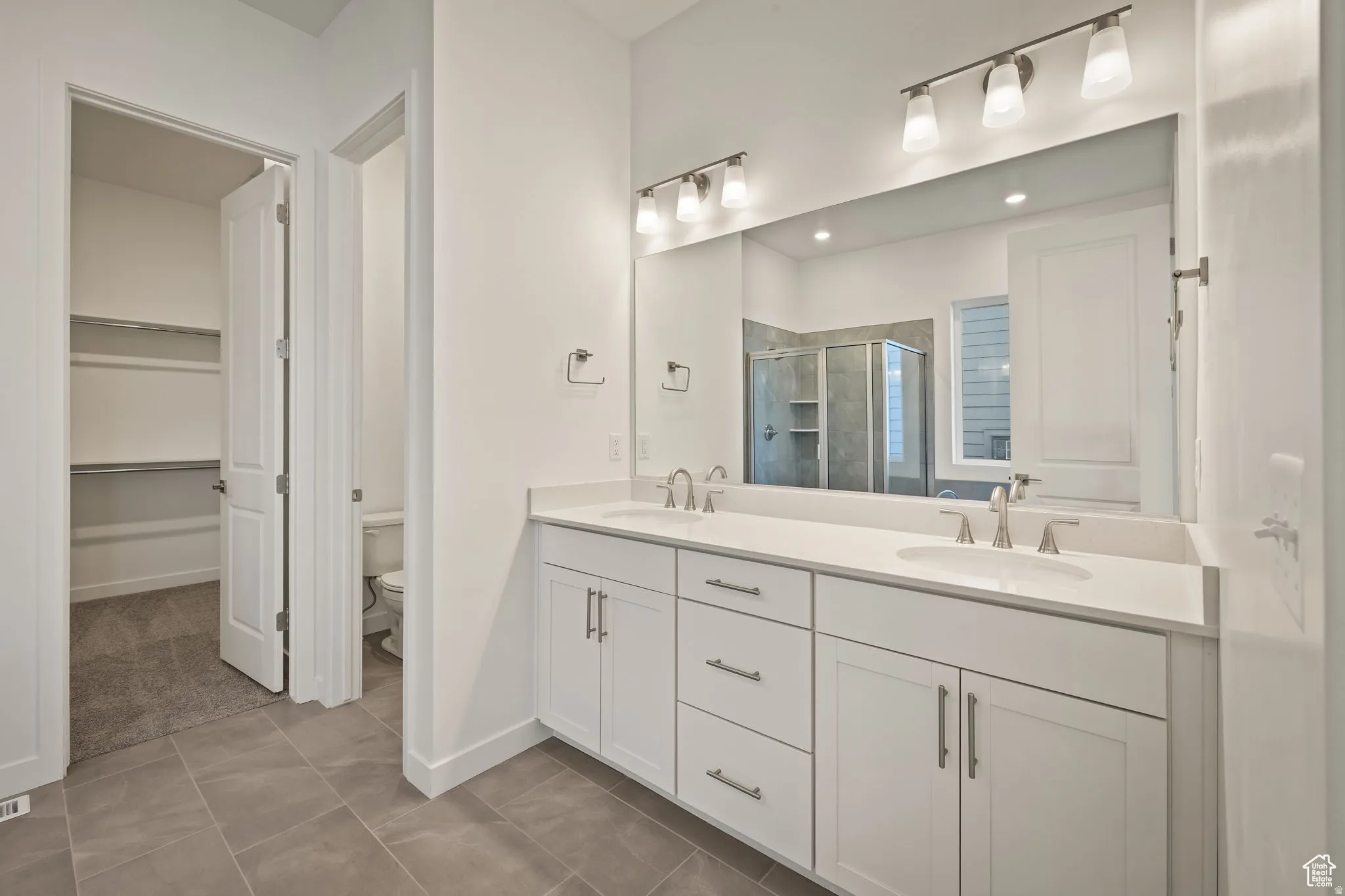 Bathroom with double vanity, a walk in closet, a stall shower, and dark tile patterned floors