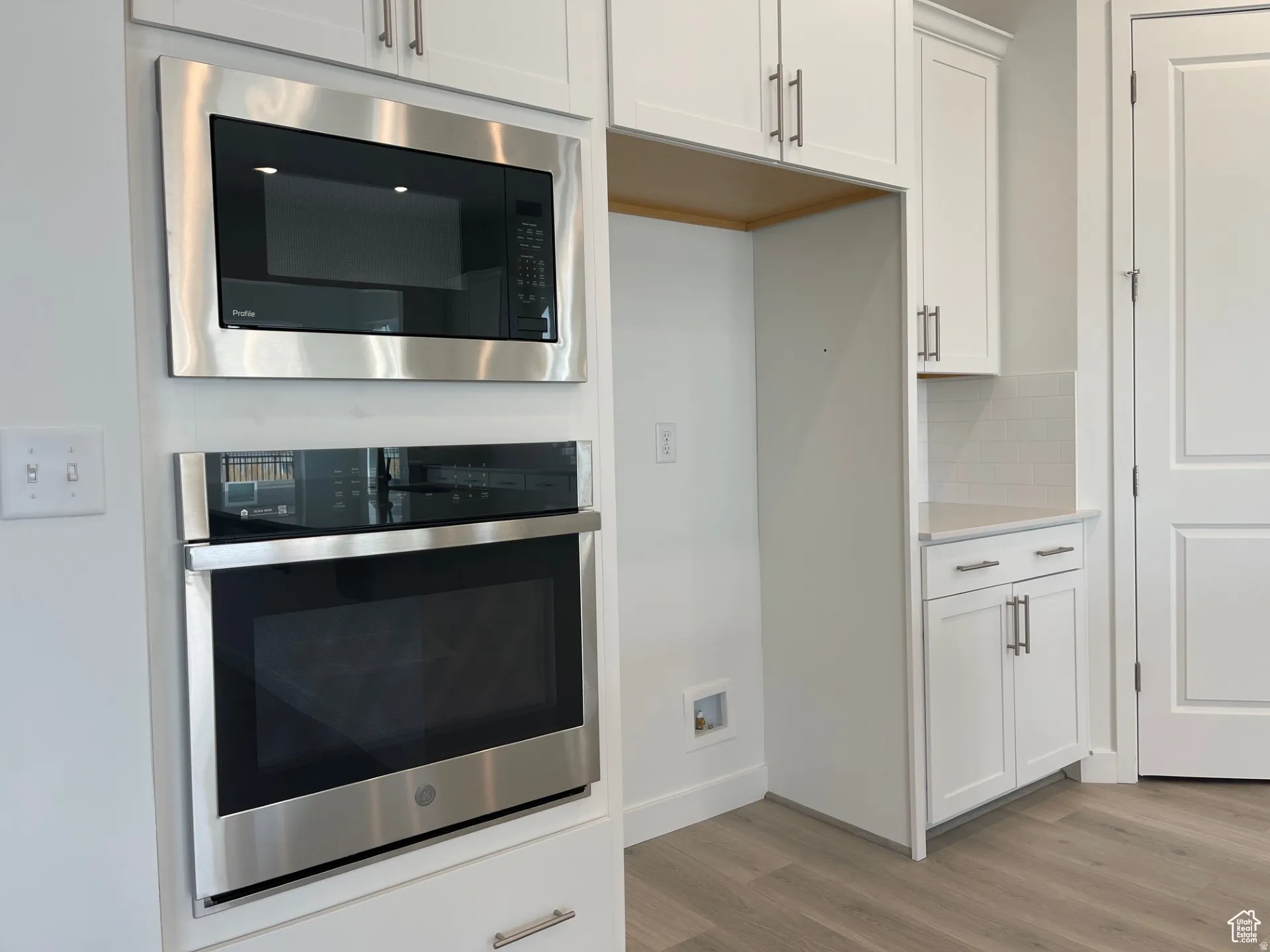Kitchen featuring stainless steel oven, white cabinetry, built in microwave, and light wood-type flooring