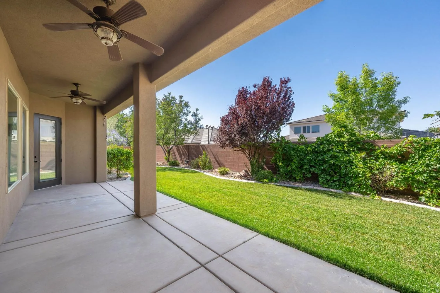 Expansive covered patio featuring ceiling fans, concrete flooring, and direct access to a manicured lawn