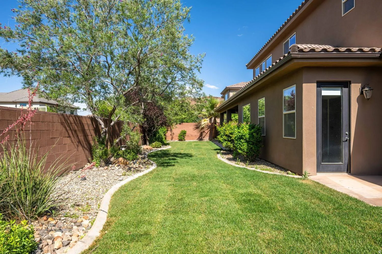 Expansive green lawn with established landscaping, featuring a mature tree, decorative rock beds, and a block perimeter fence
