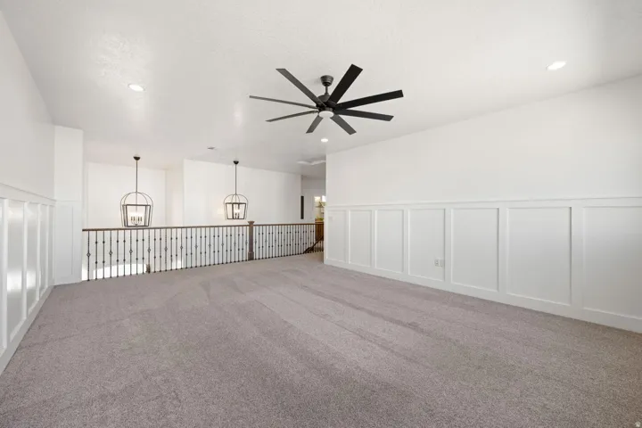 Spare room with a decorative wall, suspended lighting, a wainscoted wall, carpet flooring, and a ceiling fan