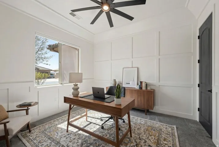 Office area with a decorative wall, carpet floors, and a ceiling fan