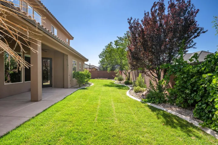 Expansive backyard featuring a manicured lawn, established landscaping, and a covered patio